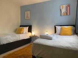 a bedroom with two beds with yellow pillows at Comfortable 3 bed House - Great Monthly Discounts in Worting