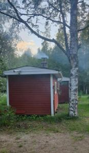 un piccolo edificio rosso accanto a un albero di Jämsän Himoksen torppa Savusaunalla a Jämsä