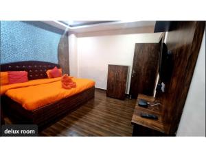 een slaapkamer met een bed met een oranje deken en een televisie bij Hotel Shri Bhagvat Dham, Chitrakoot in Sītāpur Mūāfi
