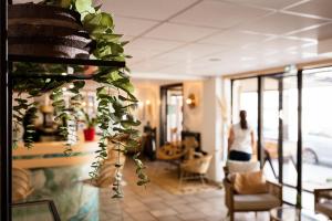a woman walking through a room with a plant at Hôtel Les Sables - Urban Style - by Logis Hotels in Canet-en-Roussillon