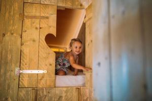 Camping Sènia Riu في سانت بير بيسكادور: فتاة صغيرة جالسة على سرير في منزل خشبي