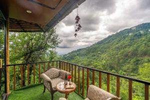 a balcony with two chairs and a table with a view at Dharamalaya by StayVista - The Eco Home in Dharamshala
