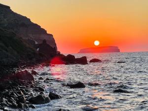 a sunset over the ocean with a rocky shore at Cave of Love Seafront Sunset View Santorini in Akrotiri