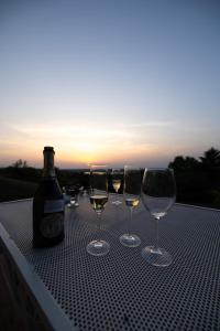 cuatro copas de vino y una botella en una mesa con la puesta de sol en Vila Krcedin en Krčedin