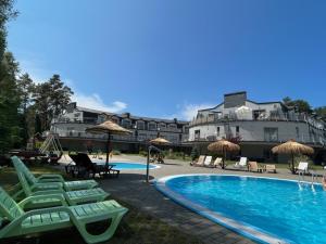 a pool with chairs and umbrellas next to a building at Apartament Baltic Meridian Pobierowo in Pobierowo