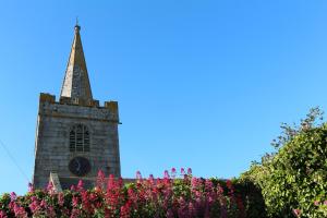 a church steeple with a tower with pink flowers at Old Temperance House B&B St Keverne in Saint Keverne