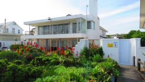 a white house with red flowers in the yard at On The Beach Apartments in Yzerfontein