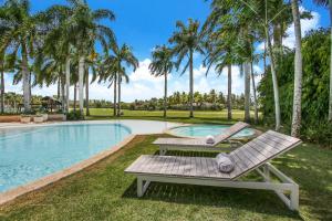 a swimming pool with two benches and palm trees at Luxurious 8-BR Villa with Ocean View, Jacuzzi, Home Cinema and Resort Access in Casa de Campo in La Romana