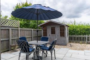 a table with chairs and an umbrella next to a dog house at 2 Bedroom Rural Escape In Peaceful Elmswell in Woolpit