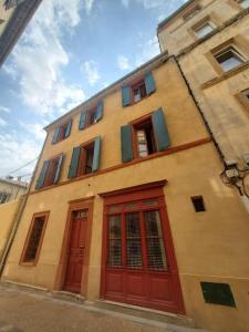 a building with red doors and windows on a street at La Louve - maison de ville in Narbonne