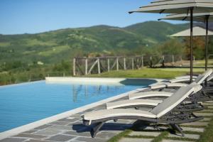 a row of white chairs and umbrellas next to a pool at Villa il Giardino - Homelike Villas in Greve in Chianti