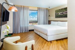 um quarto de hotel com uma cama branca e uma janela em NH HOTEL FEIRA DE SANTANA em Feira de Santana