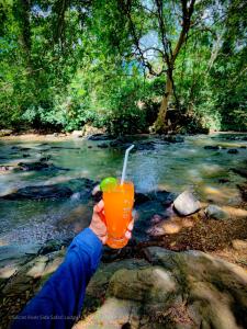 a person holding a drink in front of a stream at Secret River Side Safari Lodge in Udawalawe