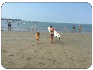 un hombre y una niña caminando por la playa con una tabla de surf en Istamboul Heist beach, en Knokke-Heist