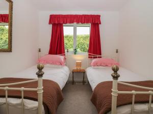 two beds in a room with red curtains and a window at The Bird's Nest in Windermere