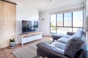 ein Wohnzimmer mit einem Sofa und einem Flachbild-TV in der Unterkunft Stones Throw To Shelly Beach, Pet Friendly! in Caloundra