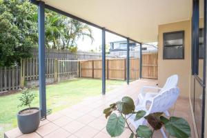 a patio with two white chairs and a plant at Stones Throw To Shelly Beach, Pet Friendly! in Caloundra