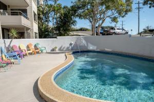 a swimming pool with colorful chairs and a fence at Retro Style Apartment Kings Beach with Ocean Views in Caloundra
