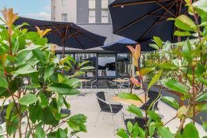 un patio avec des tables, des chaises et des parasols dans l'établissement ACE Hôtel Thionville - Porte du Luxembourg, à Thionville