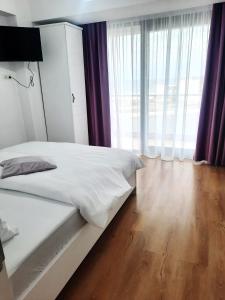 a bedroom with a bed with white sheets and a wooden floor at Apartamente Vista Lago e Mare in Eforie Nord