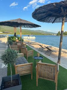 a patio with chairs and umbrellas next to the water at Apartments & Villa Tisno in Obrovac