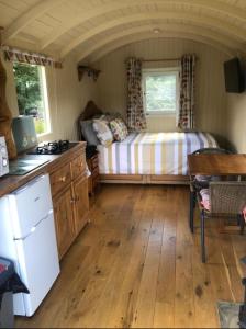 a small bedroom with a bed and a kitchen at Charming tranquil Shepherds Hut with lakeside balcony 'Roach' in Uckfield