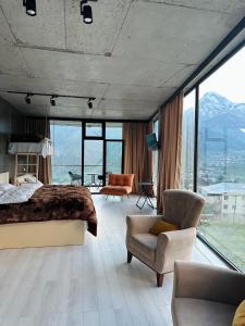 a bedroom with a bed and a chair and windows at Hotel NOA Kazbegi in Kazbegi