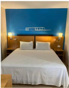 1 dormitorio con 1 cama blanca grande y pared azul en Apto no hotel Comfort de Taguatinga, en João Neiva