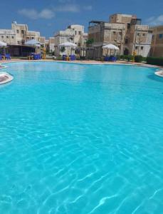 una gran piscina de agua azul con edificios al fondo en شالية عائلي بالساحل الشمالي, en Dawwār Abū Maḩrūs