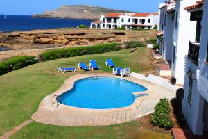 a swimming pool with two lawn chairs and two blue chairs at Apartamentos El Bergantin Menorca Club in Fornells