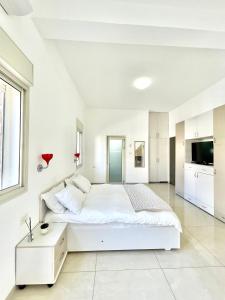 a white bedroom with a large bed and a tv at Bat Galim - by the sea in Haifa