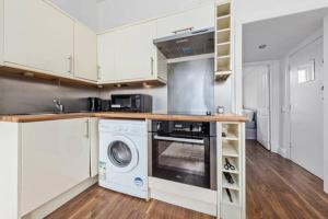 cocina con armarios blancos, lavadora y secadora en London living 2 BR Flat 2 mins to Clapahm Junction CJ, en Londres