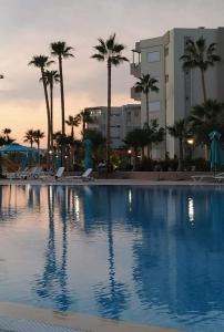 une grande piscine bordée de palmiers et un bâtiment dans l'établissement A Luxury 2BR with Big Pools Perfect for Family Summer Escape!, à Monastir