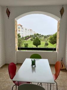 a white table and chairs in a room with a large window at Asilah Marina Golf, Appartement au calme in Asilah