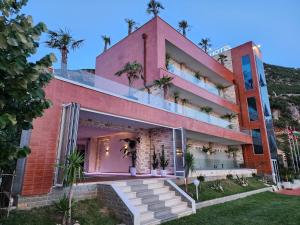 a pink building with palm trees on top of it at Festim Villa Hotel in Vlorë