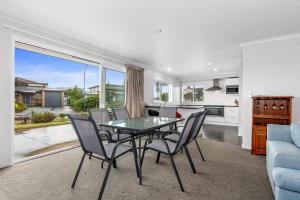 a dining room with a glass table and chairs at Shores Getaway - One Tree Point Holiday Home in One Tree Point