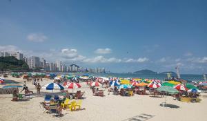 een groep mensen op een strand met parasols bij Apartamento Edifício Arpoador (Praias Asturias-Tombo) in Guarujá