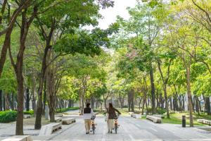 two people riding bikes down a sidewalk in a park at Hotel National in Taichung