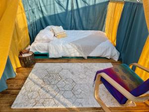 Langaland Glamping في Susenii Bîrgăului: سرير في خيمة مع كرسي وسجادة