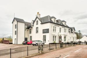 un bâtiment blanc avec des voitures garées devant lui dans l'établissement The Morar Hotel, à Morar