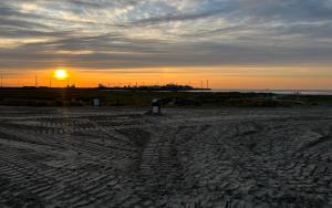 una puesta de sol en una playa con el sol a lo lejos en Istamboul Heist beach en Knokke-Heist