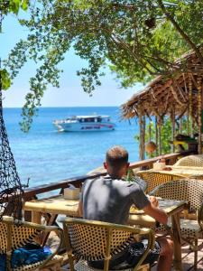 a man sitting at a table watching a boat in the water at Haadson Resort & Koh Raham in Haad Son