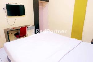 Hotel Permata Makassar Mitra RedDoorz في Balangberu: غرفة نوم بسرير ابيض وكرسي احمر