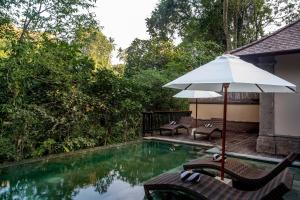 a swimming pool with an umbrella and chairs and a table at The Lokha Ubud Resort, Villas & SPA in Ubud