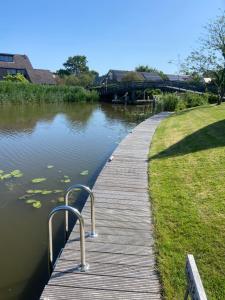 a wooden boardwalk next to a lake with a house at Wetterwillefriesland in Wommels