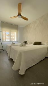 two beds in a white room with a ceiling fan at Urbanlux Belmonte Suite in Albacete