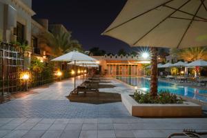 a swimming pool with tables and umbrellas at night at Andalus Al Seef Resort & Spa in Abu Dhabi