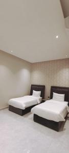 twee bedden in een kamer met witte muren bij شاليهات أبيات الفندقية in Al Baha