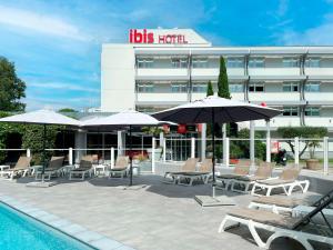 una piscina con sillas y sombrillas frente a un hotel en ibis Nîmes Ouest - A9 en Nimes