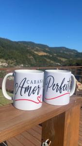 two coffee mugs sitting on top of a wooden rail at Cabana Amor Perfeito in Alfredo Wagner